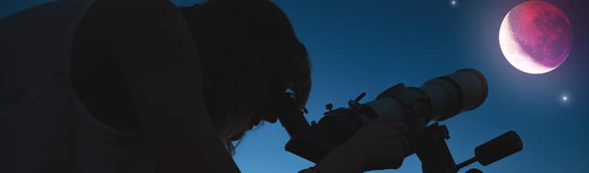 A silhouette is looking at the Moon through a telescope.