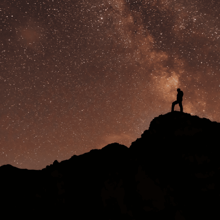 man on a hill starring at the stars