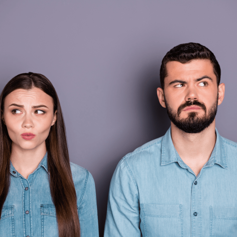 A couple in denim shirts stand next to each other, looking away with consternated expressions on their faces.