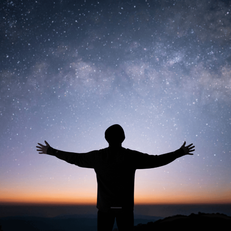 silhouette of a man with arms outstretched starring up at a blue starry sky