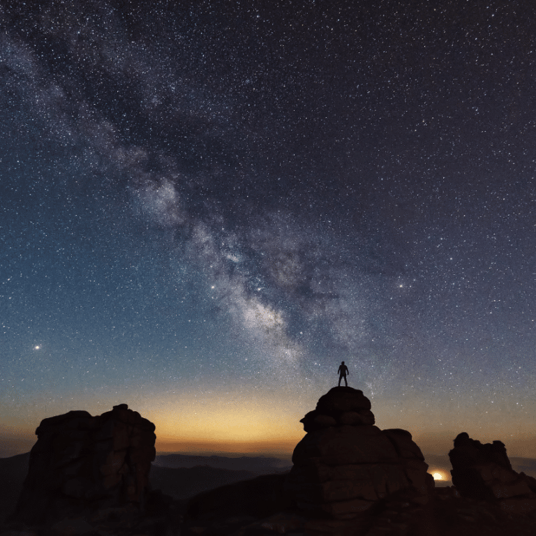 man in the distance standing on a hill starring at the night sky