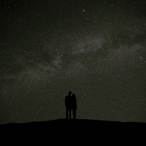 couple standing on a hill looking at a green starry night