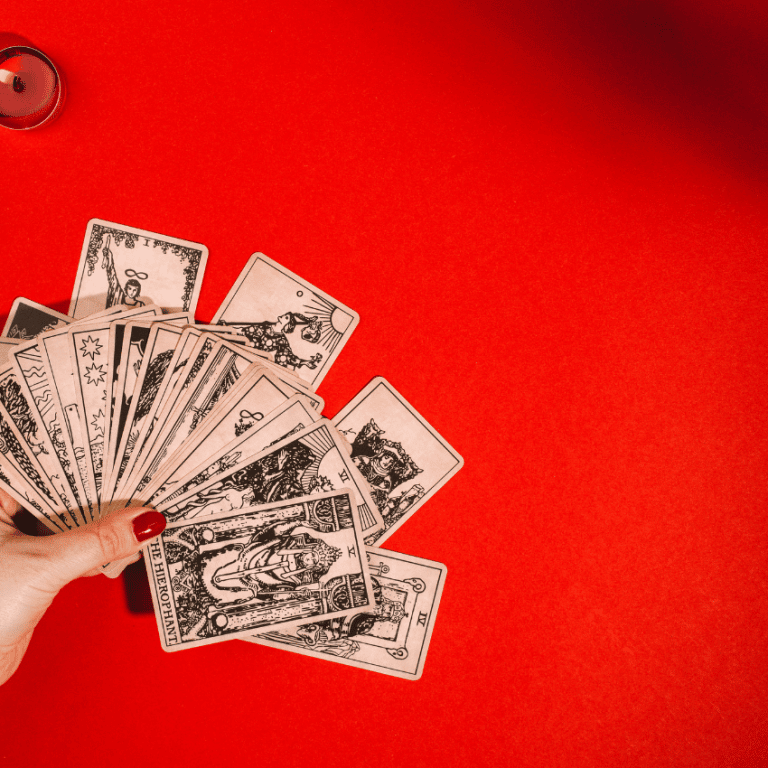 pair of hands holding a handful of tarot cards above a red table