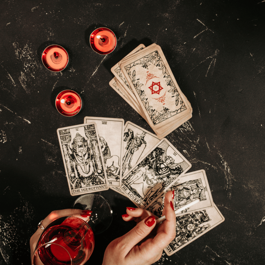 tarot cards spread across a black table with a pair of hands holding a glass of wine