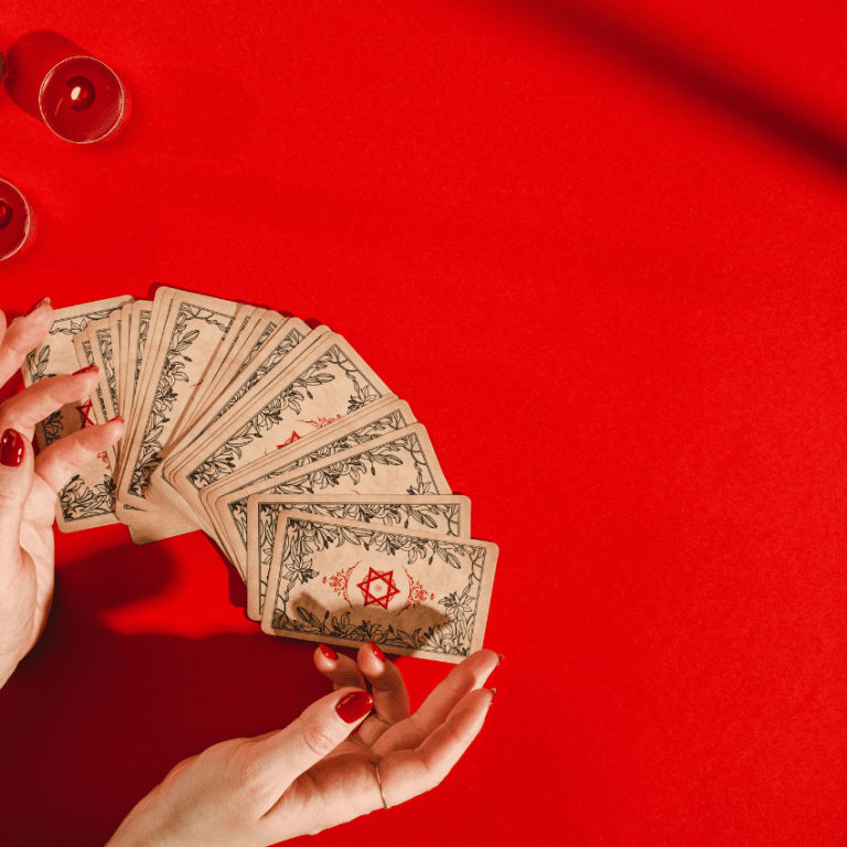 pair of hands gesturing to a deck of tarot cards spread out on a red table