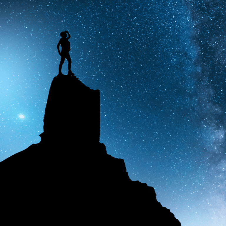 silhouette of a person standing on mountain gazing up at a starry blue sky