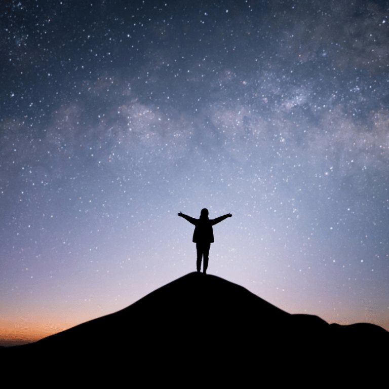 person standing on a hill with arms outstretched against a grey and blue starry sky