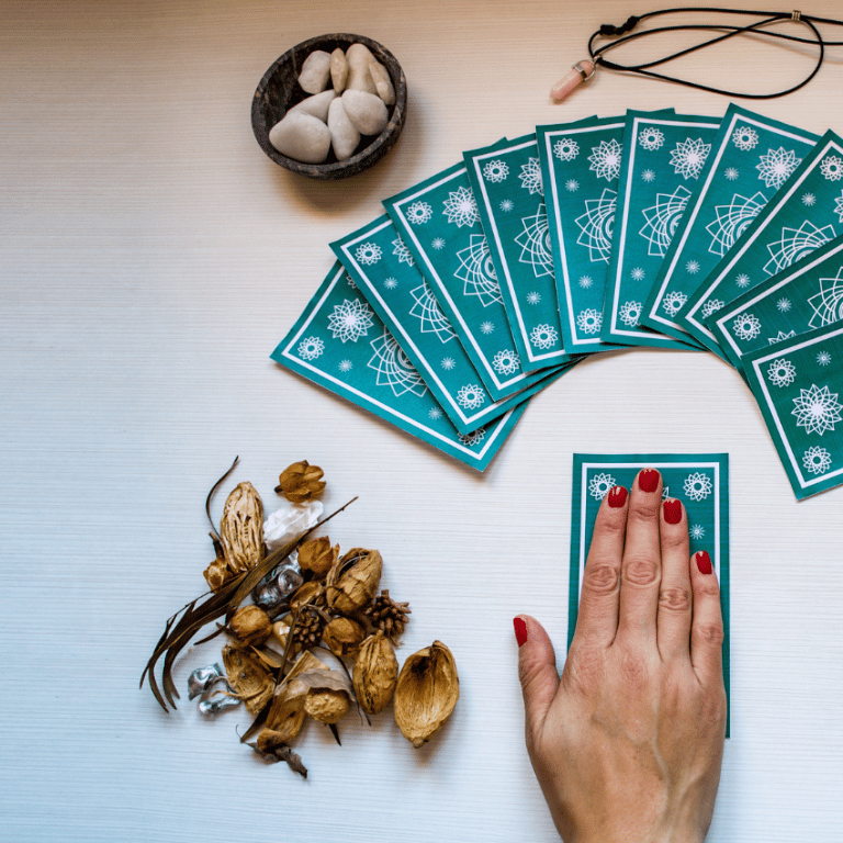 hand over top of a blue tarot card on a white table with other tarot cards and crystals spread out