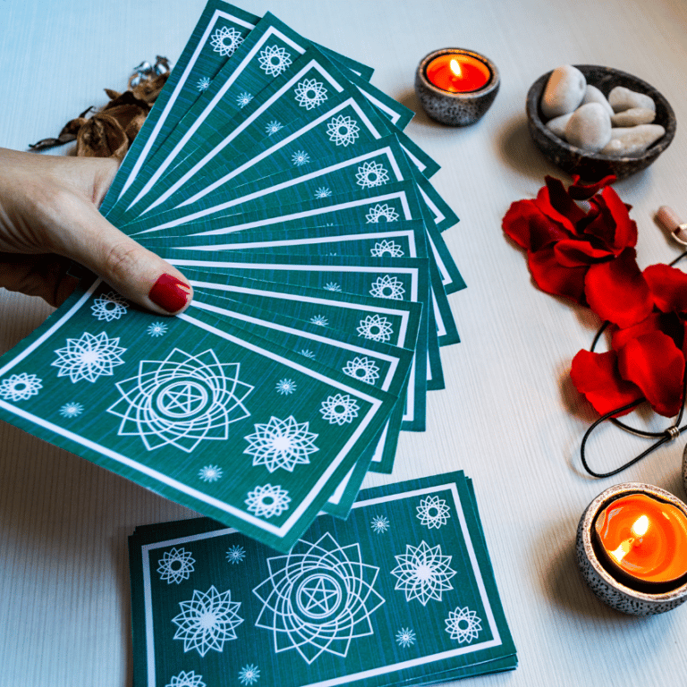 hand holding out a spread of blue tarot cards over a white table with candles and rose petals