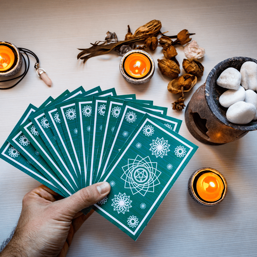 hand holding an array of blue tarot cards over top of a white table with candles and crystals