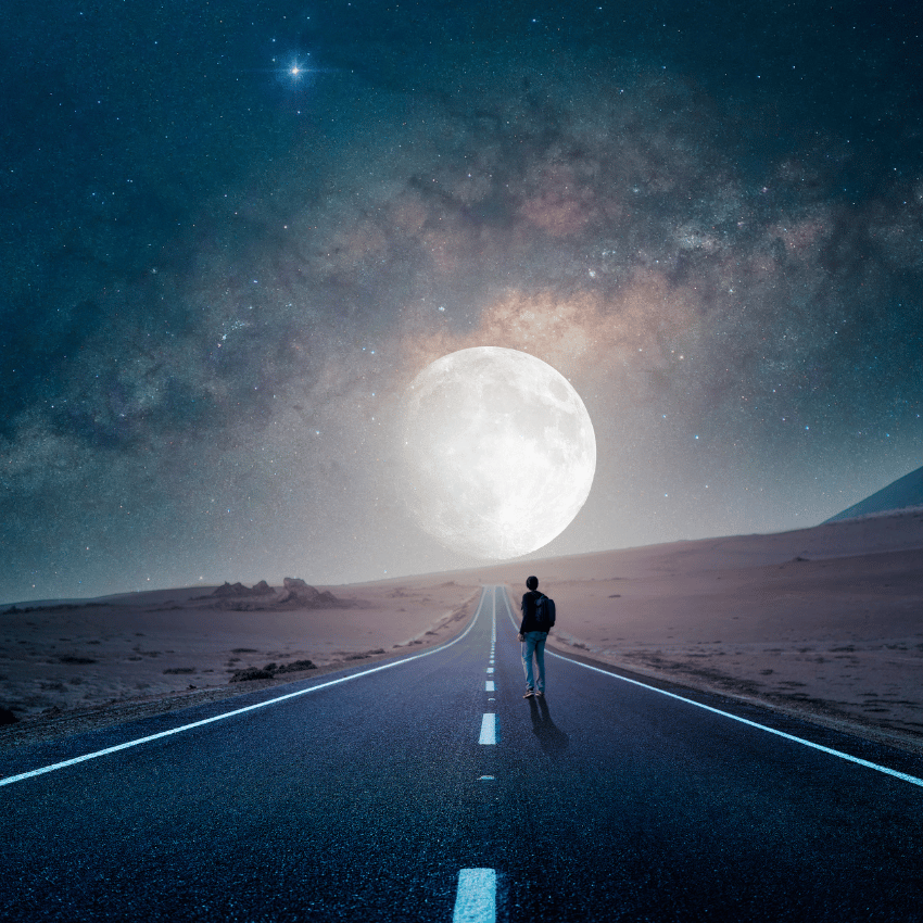 man standing on a deserted street staring at a large moon in the night sky