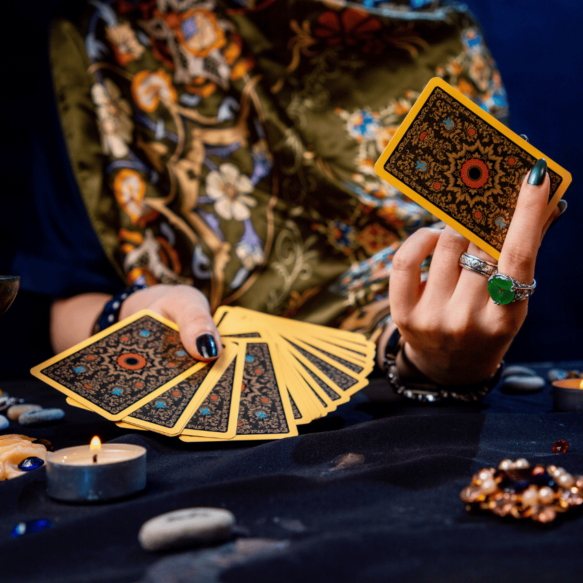 hands adorned with rings holding up gold and black tarot cards