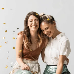 two woman hugging and smiling as gold and silver confetti fly around them