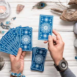 pair of hands holding blue tarot cards over a white table covered in crystals and wood