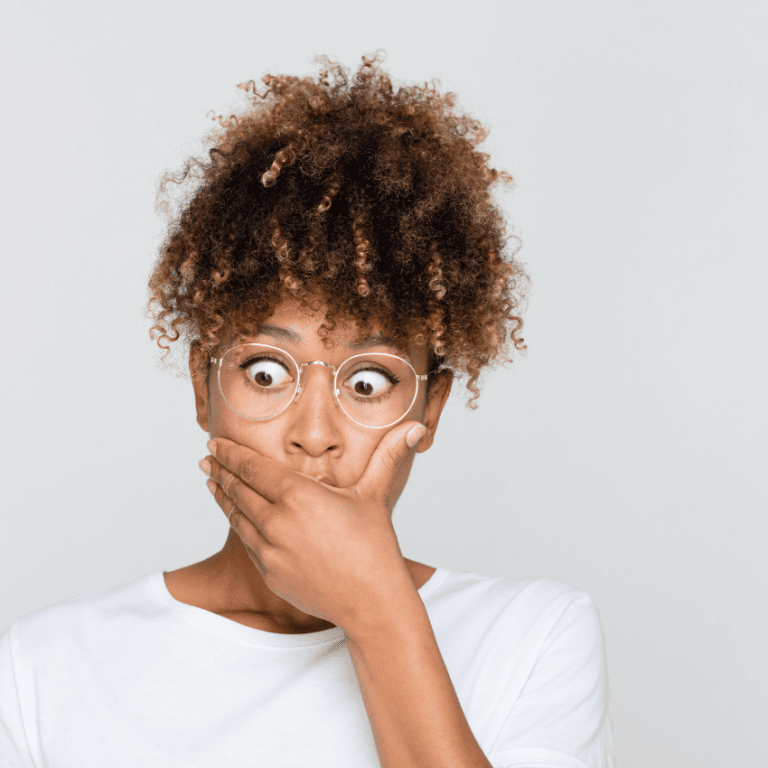 woman with glasses staring ahead looking shocked with her hand over her mouth