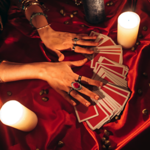 an array of red tarot cards being spread out on a red cloth surrounded by candles