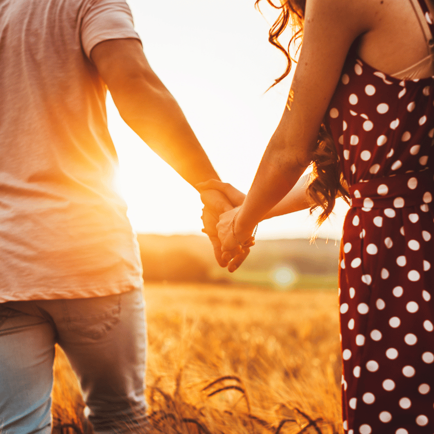 couple holding hands in a field with the sun setting