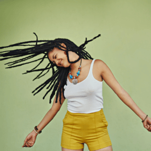 woman with dreadlocks, a white tank top, and yellow shorts dancing around joyfully