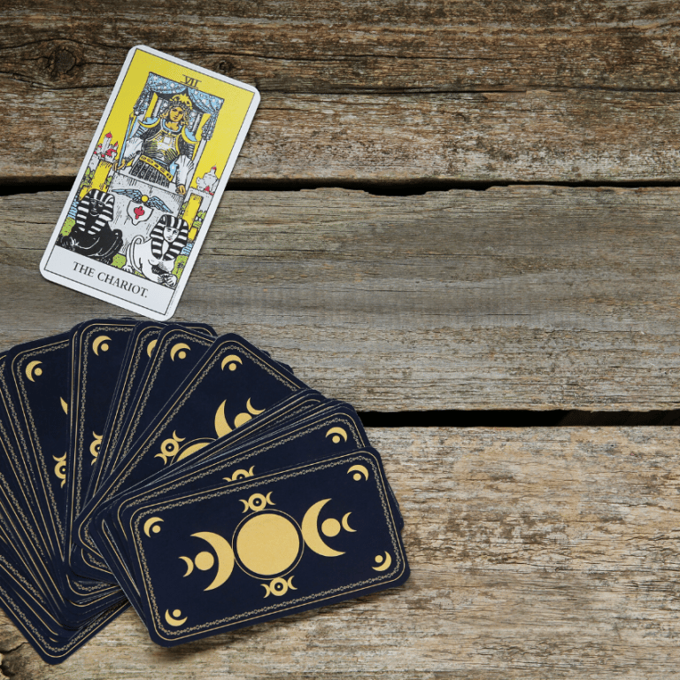 the chariot tarot card laid on a wooden table beside a dark blue and gold tarot deck