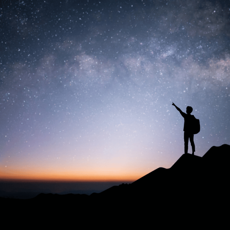 silhouette of a person standing on a hill pointing at a blue starry night