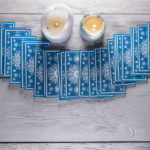 blue tarot cards spread out on a grey table with two candles