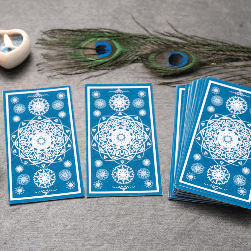 blue tarot cards spread out on a grey table with feathers and a candle