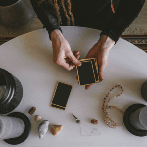 pair of hands dealing out a deck of black and gold tarot cards on a white table with crystals and candles