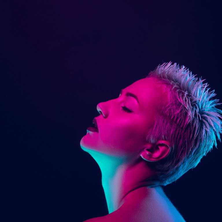 woman with a white mohawk gazing up with her eyes closed against a dark blue background