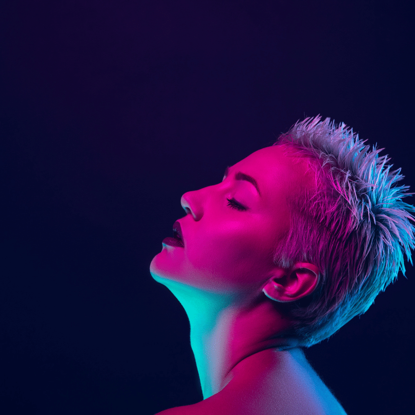 woman with a white mohawk gazing up with her eyes closed against a dark blue background