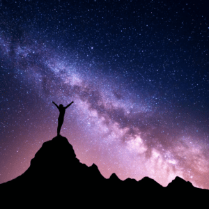 black silhouette of a person standing on a large hill with their arms outstretched toward a purple and blue starry sky