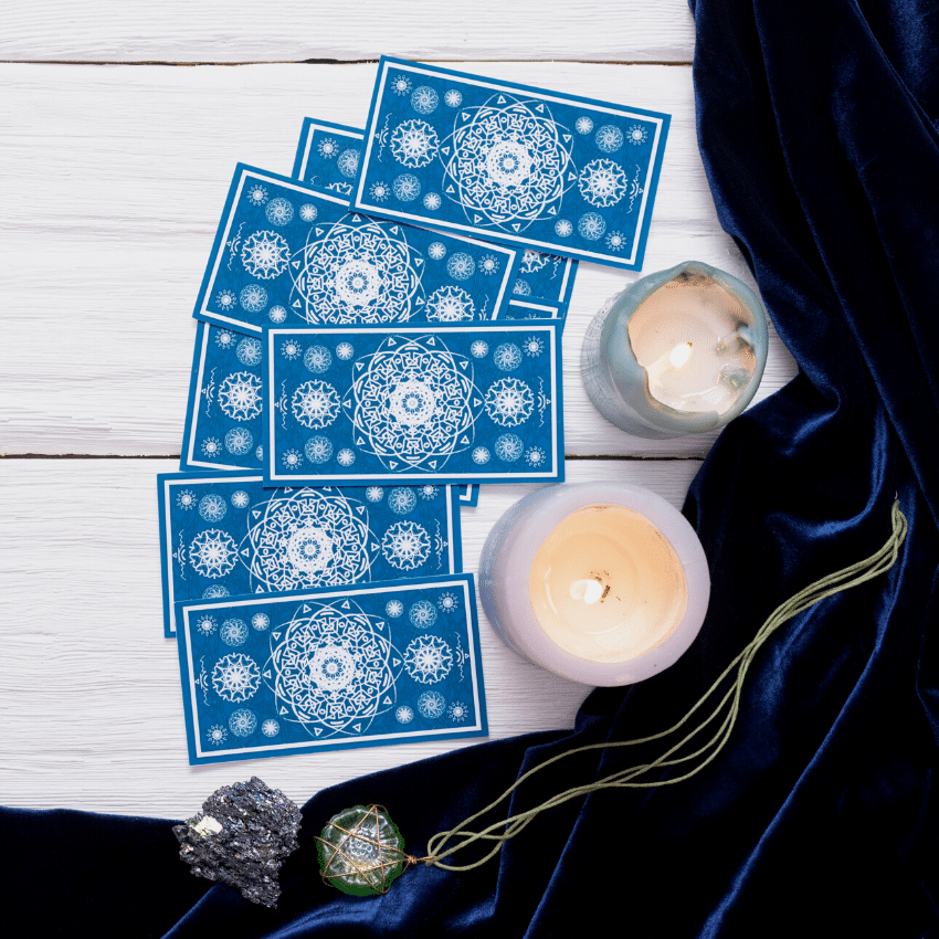 blue tarot cards spread out on a white wooden table surrounded by candles and a black cloth