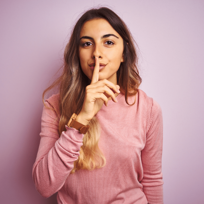 brunette woman holding a finger up to her lips against a pink background