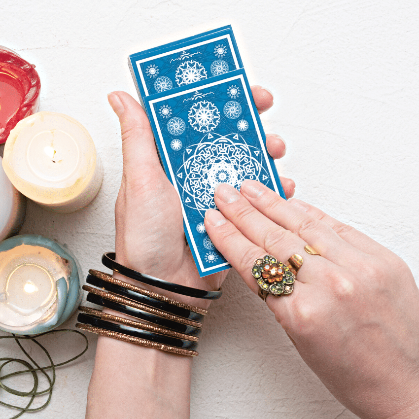 pair of hands adorned with rings and bracelets holding a stack of blue tarot cards