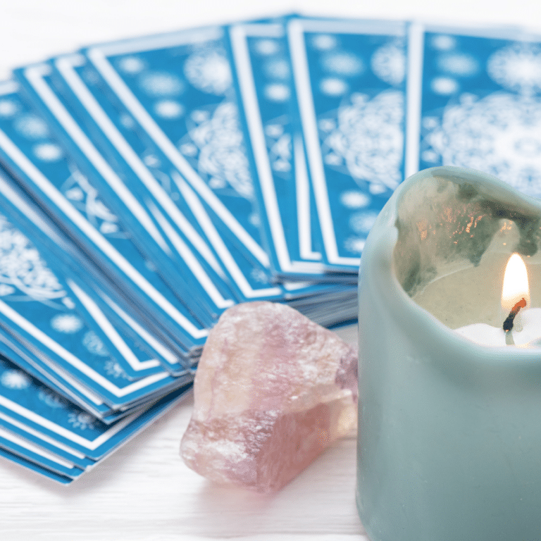 blue tarot cards beside a blue candle and a pink crystal on a white wooden table