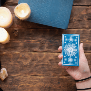 a hand holding out a blue tarot card over a wooden table covered in candles