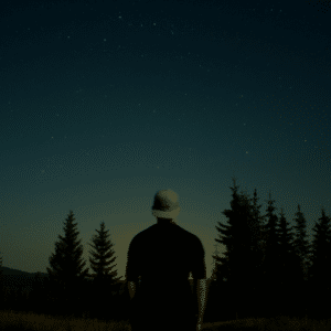 man in a baseball cap looking out to a forest full of trees and a blue starry sky
