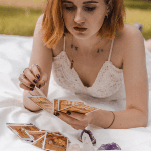 woman in a white shirt with short red hair laying on a white blanket reading tarot cards