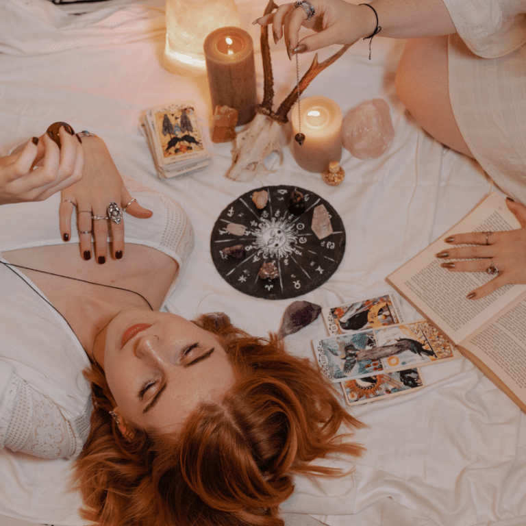woman with red hair lying down surrounded by esoteric items such as tarot cards and crystals