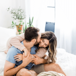 couple sitting on a bed hugging each other and smiling with plants in the background