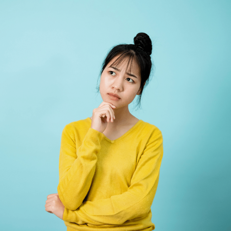 asian woman with black hair and a yellow sweater looking contemplative