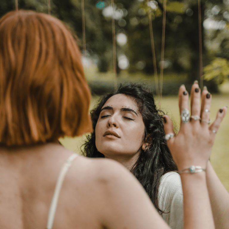 two women in nature holding up their hands together with their eyes closed in some sort of ritual