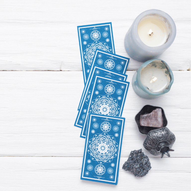 five blue tarot cards spread on a white wooden table with candles and crystals