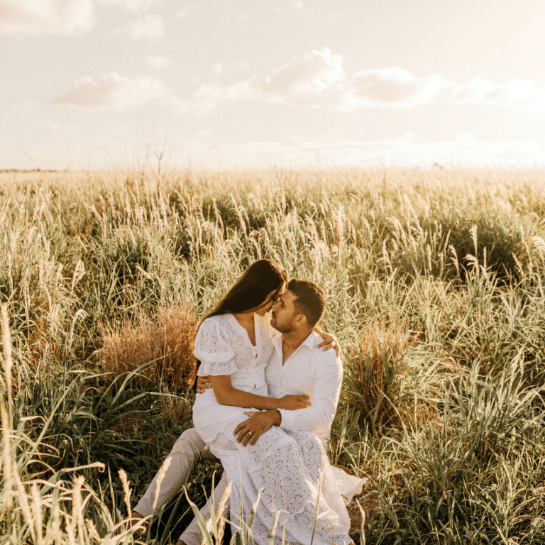 couple in a field of grass dressed in white embracing each other and staring at each other lovingly