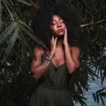 woman with afro with closed eyes looking serene surrounded by lush greenery