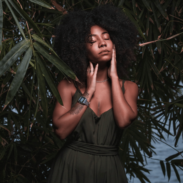 woman with afro with closed eyes looking serene surrounded by lush greenery