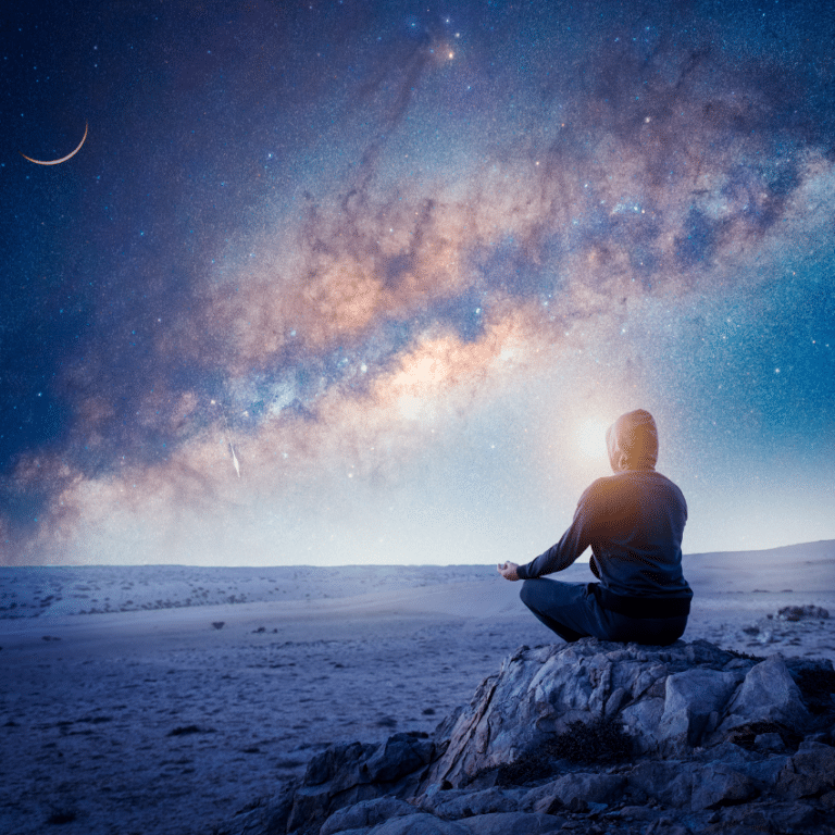 man sitting on a grey rock in a lotus pose meditating while a purple and blue sky sparkles with stars above him