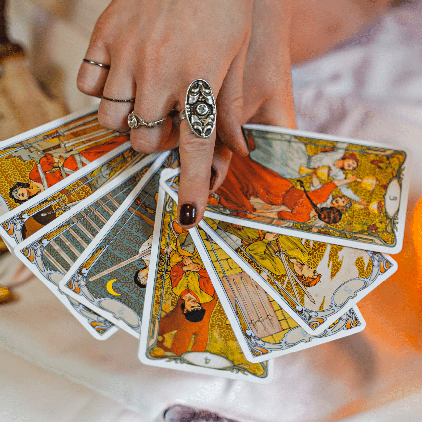 hand adorned with rings holding out a selection of colourful tarot cards