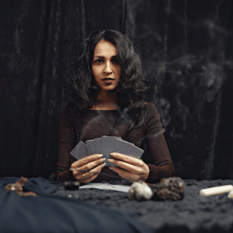 woman with dark hair holding a spread of black tarot cards staring ahead