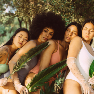 four women leaning into each other with their eyes closed in nature