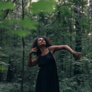woman in a black dress dancing freely through a green forest
